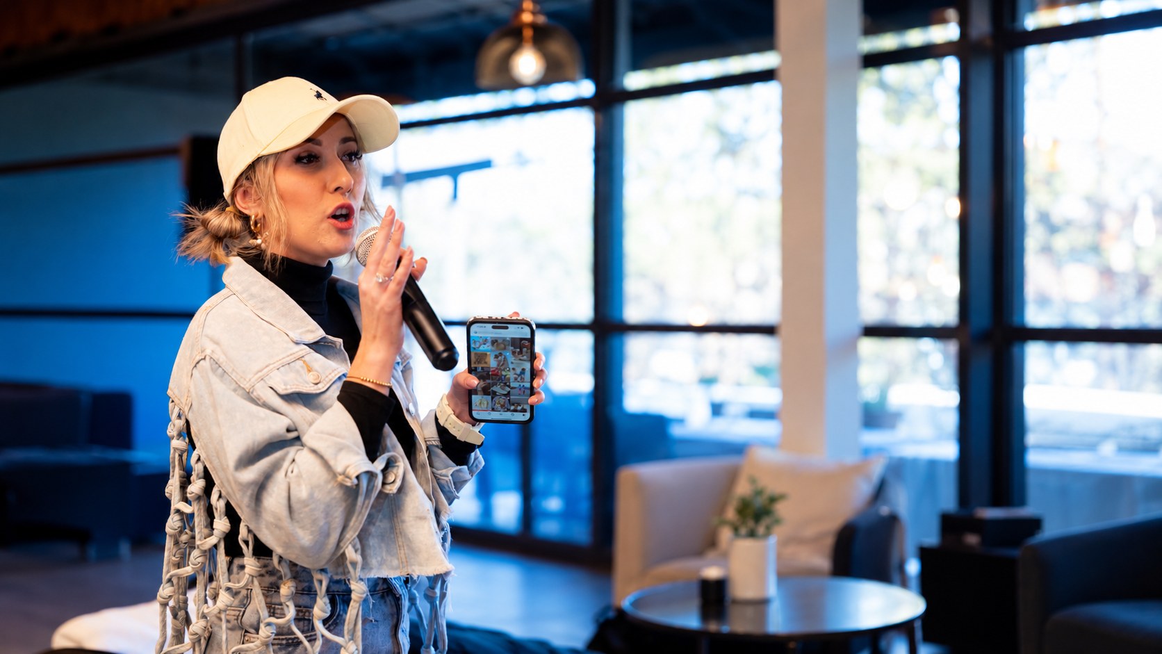 Danielle Steynvaardt teaching a School of Influence session, holding a microphone and a phone showing an Instagram feed